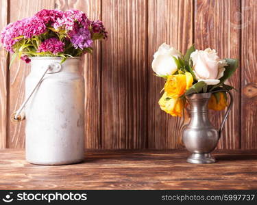 Bouquet of pink carnations in a vintage tin can on wooden background. Rustic decorative setting