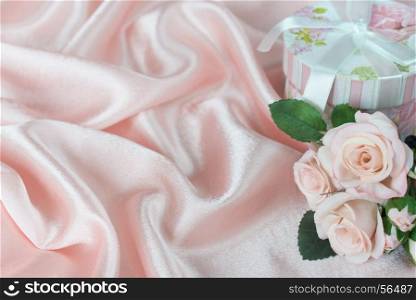 Bouquet of pink roses and gift box with bow on a background of wavy pink silk fabric