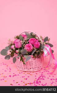 Bouquet of pink roses in a wicker basket on a pink table background. Birthday, Wedding, Mother’s Day, Valentine’s Day, Women’s Day. Front view