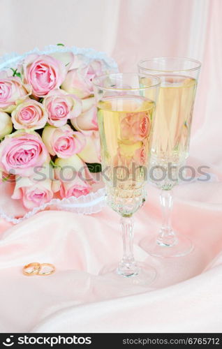 Bouquet of pink roses, wedding rings and two glasses of white wine on satin fabric background