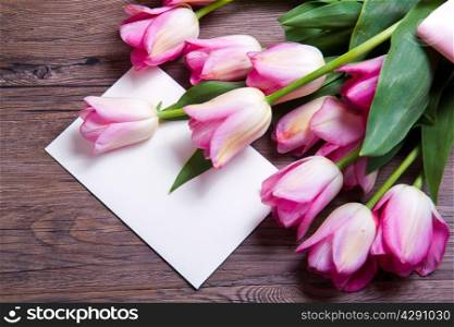 bouquet of pink tulips and postcard on wood