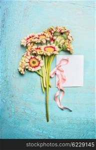 Bouquet of pretty flowers with bow and white blank card on turquoise shabby chic background, top view