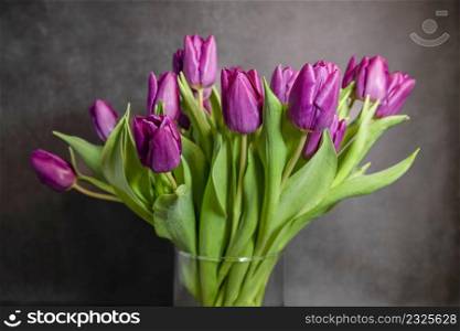 bouquet of purple flowers in a glass vase with a dark background. a bouquet purple dutch tulips in a vase