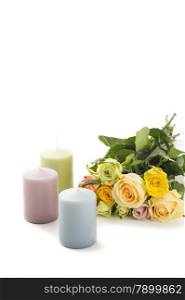 Bouquet of roses with a trio of pretty pastel candles to celebrate Valentines Day, Mothers Day or an anniversary arranged on a white background with copyspace for your greeting for a loved one
