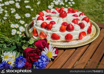 Bouquet of summer flowers at a table with homemade strawberry cake in a garden