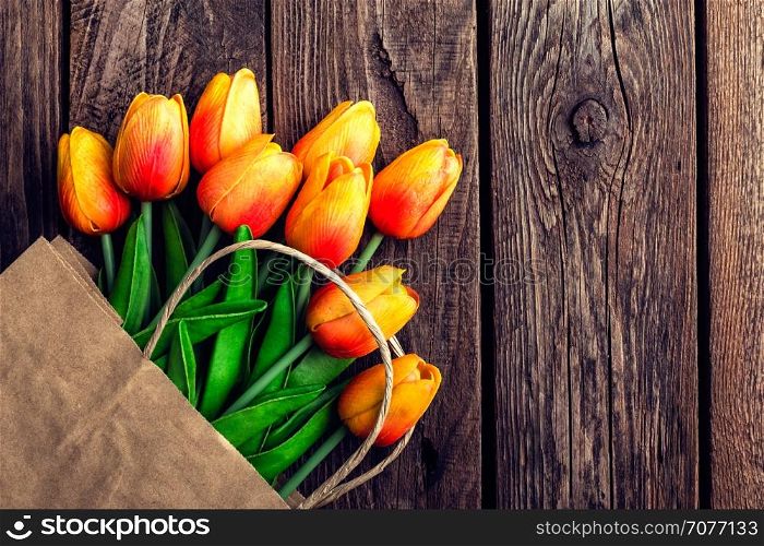 Bouquet of tulips in a paper shopping bag on a wooden background, concept of discounts and sales on the Women's Day or Mother's Day or Easter