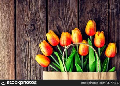 Bouquet of tulips in a paper shopping bag on a wooden background, concept of discounts and sales on the Women's Day or Mother's Day or Easter