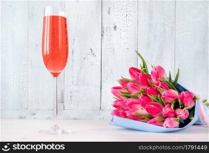 Bouquet of tulips with glass of champagne on the wooden background