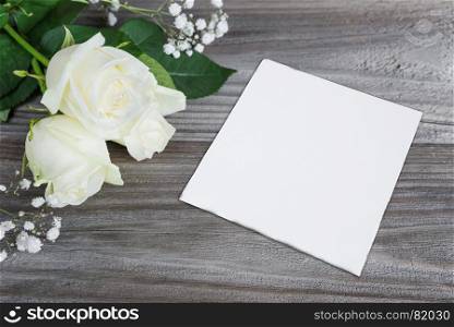 Bouquet of white rose flowers and white paper card are on the gray background of old wooden boards, with space for text