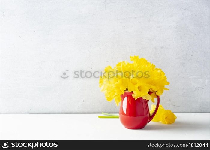 Bouquet of yellow daffodils in a red jug on table top, home decor, interior, copy space