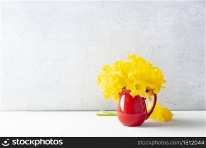Bouquet of yellow daffodils in a red jug on table top, home decor, interior, copy space