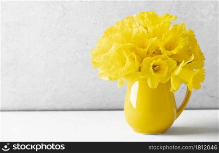 Bouquet of yellow daffodils in a yellow jug on table top, home decor, interior, copy space