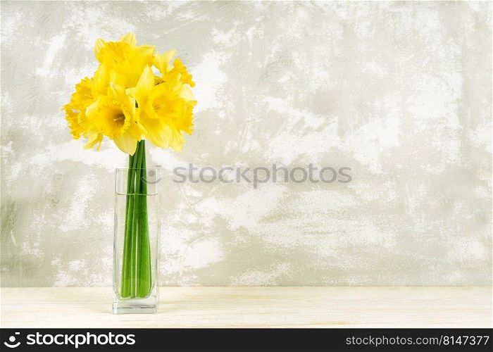Bouquet of yellow daffodils, narcissus in transparent vase on aged white plaster background with copy space. Mockup, template for holiday, birthday, mother’s day on yellow background with copy space. Bouquet of yellow daffodils, narcissus in vase on white plaster background with copy space
