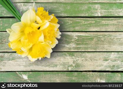 Bouquet of yellow daffodils, narcissus on green wooden background with copy space. Mockup, template for holiday, birthday, mother’s day on yellow background. Top view, flat lay with copy space. Bouquet of yellow daffodils, narcissus on green wooden background with copy space