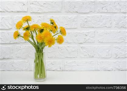 Bouquet of yellow dandelion in vase on table background white brick wall Copy space Minimal style. Template for postcard, text, design Concept Women's day, Mothers Day, Hello summer or Hello spring.. Bouquet of yellow dandelion in vase on table background white brick wall Copy space Minimal style. Template for postcard, text, design Concept Women's day, Mothers Day, Hello summer or Hello spring