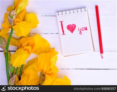 bouquet of yellow irises and a notebook with an inscription red pencil on a white wooden background