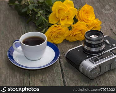 bouquet of yellow roses, cup of coffee and a retro the camera on a table