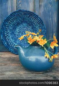 Bouquet of yellow wild flowers in a blue clay pot, on the blue wooden background. Still life in rustic style. Beauty, Nature, Simple. Countryside lifestyle, weekend, vacation, breakfast concept