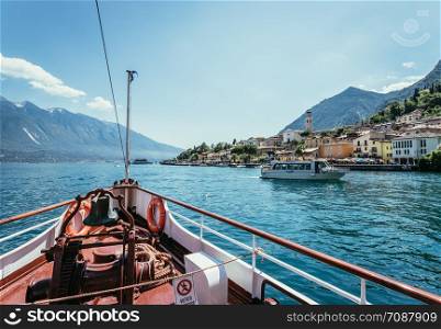 Bow of a boat on a boat tour. Blue water, moutnain range and little village, Lago di Garda, Italy