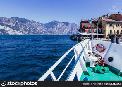 Bow of a boat on a boat tour. Blue water, mountain range and little village, Lago di Garda, Italy