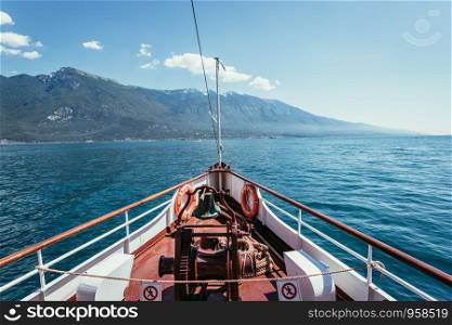 Bow of a boat on a boat tour. Blue water, moutnain range and little village, Lago di Garda, Italy