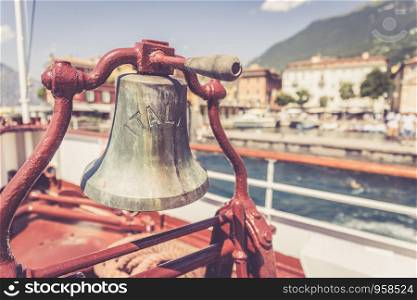 Bow of a boat with boat bell on a cruise tour. Blue water, mountain range and cute little village at Lago di Garda, Italy