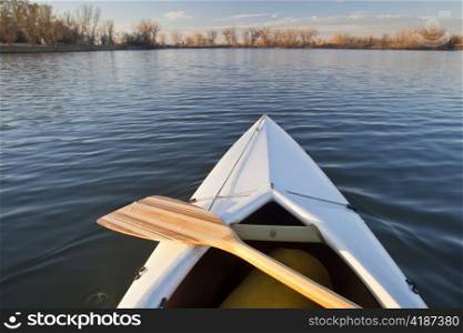 bow of white canoe with wooden paddle on a calm lake in Colorado