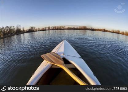 bow of white decked canoe with wooden paddle on a calm lake in Colorado - a fish eye lens perspective