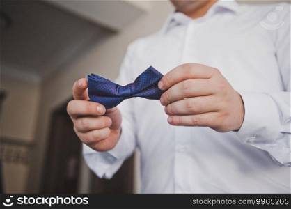 Bow tie in the hands of the groom.. A man in a white shirt is holding a bow tie 2322.