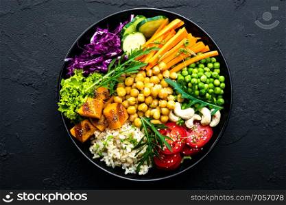 Bowl dish with brown rice, cucumber, tomato, green peas, red cabbage, chickpea, fresh lettuce salad and cashew nuts. Healthy balanced eating