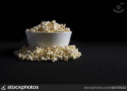 Bowl filled with popcorns kept over a black background. 