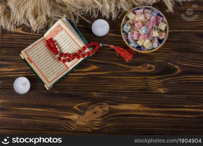 bowl multicolored lukum red holy rosary beads kuran with candles wooden surface. Beautiful photo. bowl multicolored lukum red holy rosary beads kuran with candles wooden surface