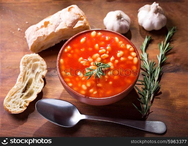 bowl of bean soup with rosemary on wooden table, top view