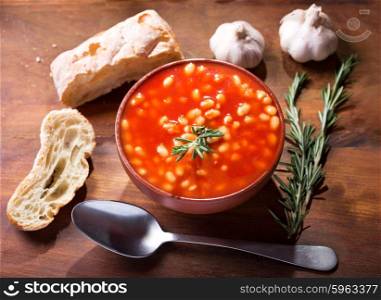 bowl of bean soup with rosemary on wooden table, top view