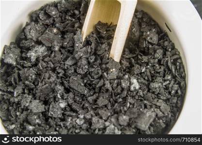 Bowl of black charcoal sea salt, in white ceramic bowl with wooden scoop close up or macro, background