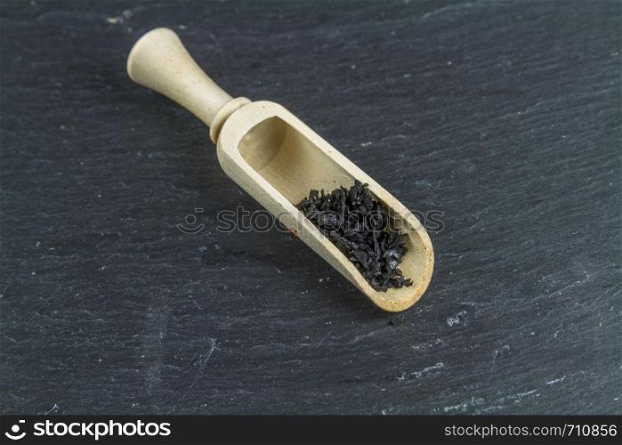 Bowl of black charcoal sea salt, in wooden scoop or macro, background