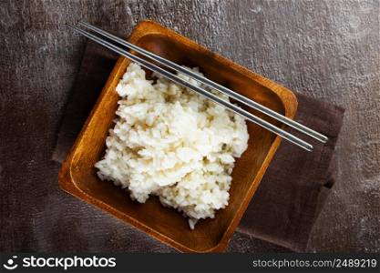 Bowl of boiled rice and sticks on dark table