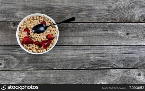 Bowl of breakfast cereal with milk and fresh strawberries on an old wooden table