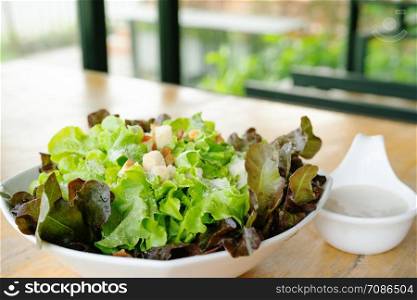 Bowl of Caesar Salad with dressing on wooden table