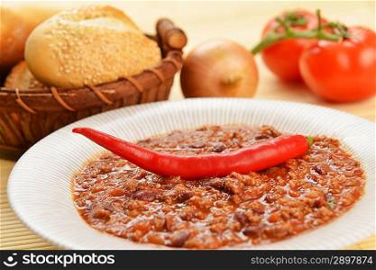 Bowl of chili with peppers, beans and basket of bun