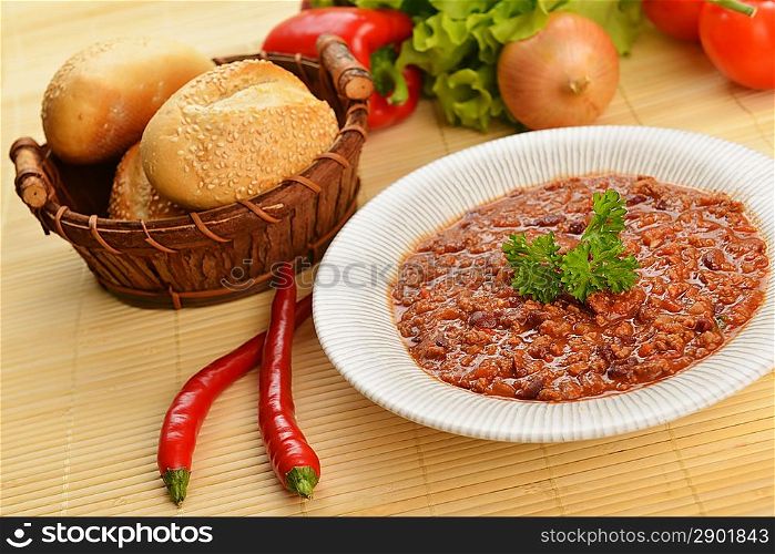 Bowl of chili with peppers, beans and basket of bun