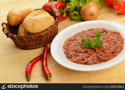 Bowl of chili with peppers, beans and basket of bun