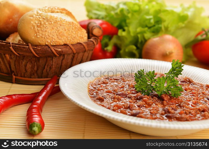 Bowl of chili with peppers, beans and basket of bun