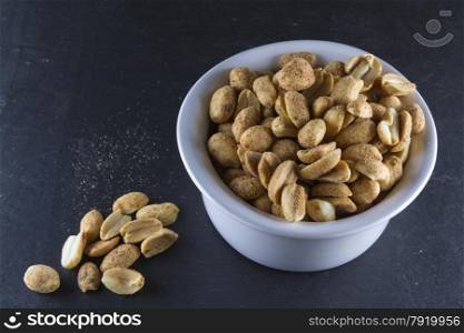 Bowl of dry roast peanuts on slate mat, some on slate.