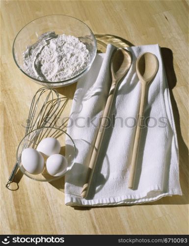 Bowl of flour near a whisk and eggs