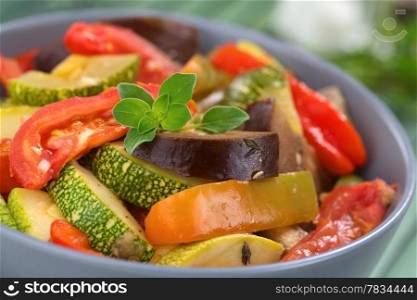 Bowl of fresh homemade Ratatouille made of eggplant, zucchini, bell pepper and tomato and seasoned with herbs (garlic, thyme, oregano), garnished with fresh oregano (Selective Focus, Focus on the oregano leaves on the meal). Ratatouille