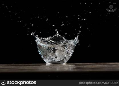bowl of glass with water bursting on a wood table in a dark ambient