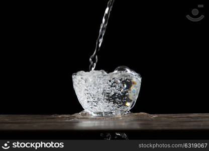 bowl of glass with water falling on a wood table in a dark ambient