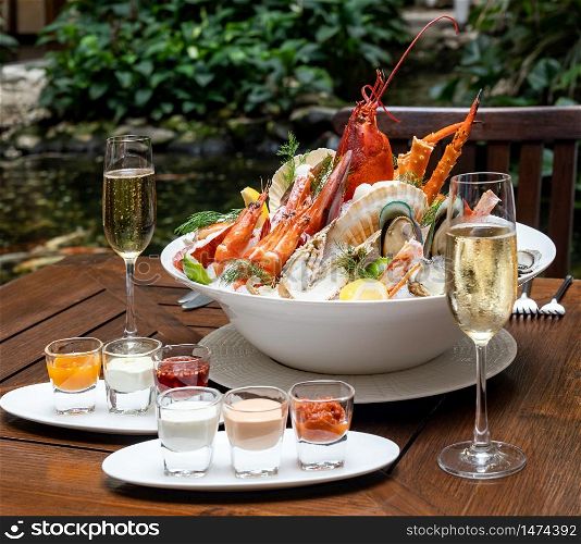 Bowl of gourmet fresh seafood on ice with savory sauce serve with white wine glass on vintage wooden table. Restaurant gastronomy food and drink consumerism concept.