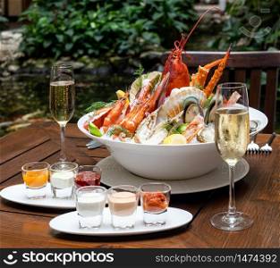Bowl of gourmet fresh seafood on ice with savory sauce serve with white wine glass on vintage wooden table. Restaurant gastronomy food and drink consumerism concept.